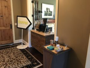 La Vita Espresso mobile coffee cart setup at an indoor grad party, featuring a rustic wooden cart with an espresso machine and a large coffee grinder. A bright 'Coffee' sign directs guests to the coffee station, while a side table is stocked with napkins, stirrers, sugar, and cups. The setup offers a cozy, professional coffee catering experience for events in Minneapolis, St. Paul, and the Twin Cities.